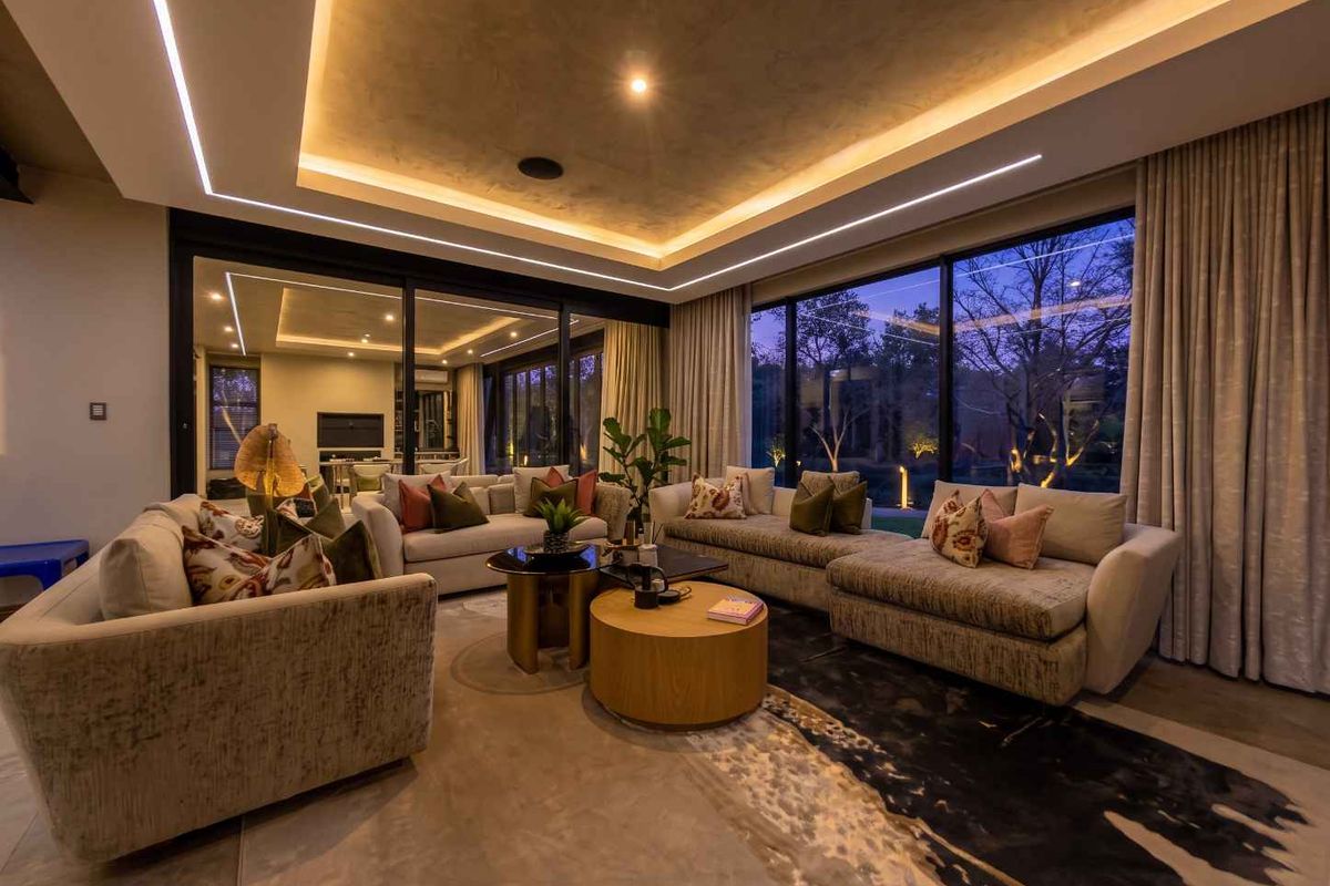 Modern living room featuring a sophisticated recessed tray ceiling with integrated LED lighting, polished concrete floors, and expansive sliding glass doors opening to the garden.
