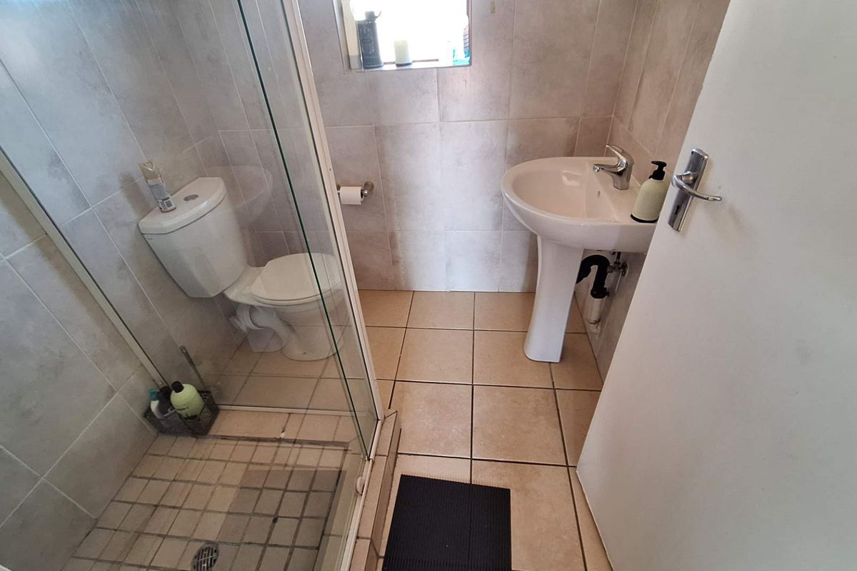 A functional bathroom featuring a pedestal washbasin, a toilet, and a glass-enclosed shower with neutral ceramic tiling throughout.