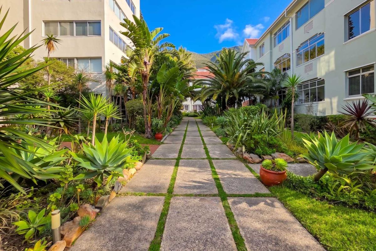 A well-maintained central courtyard garden featuring a paved walkway flanked by lush tropical landscaping and apartment building facades.