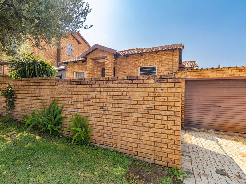 Front exterior view of a face brick townhouse featuring a paved driveway, private boundary wall, and a secure roller garage door.