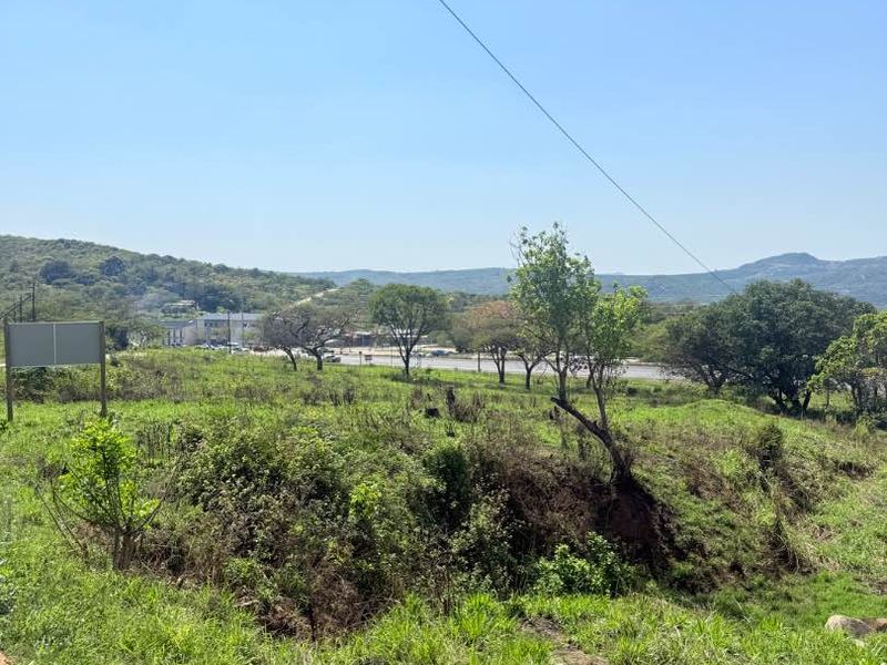 A view of a vacant residential plot featuring natural vegetation, sloped terrain, and surrounding landscape views.