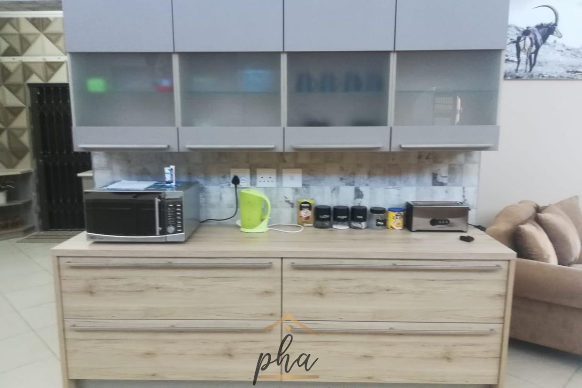 Modern kitchen cabinetry featuring light wood-grain base units, grey overhead cupboards with glass inserts, and a neutral tiled backsplash.