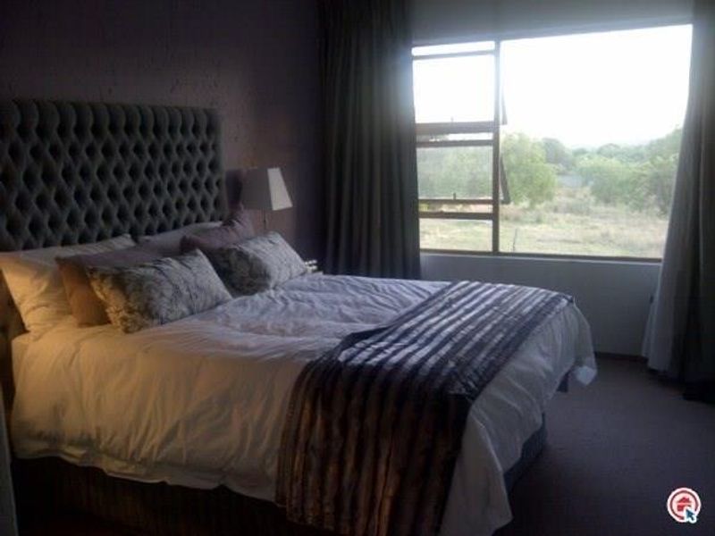 A bedroom featuring carpeted flooring and a large window with natural light, offering a view of the surrounding landscape.