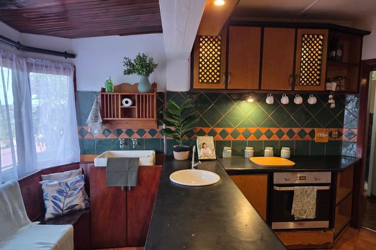 A rustic-style kitchen featuring dark timber cabinetry, a farmhouse sink, integrated oven, and a decorative tiled backsplash with a warm, lived-in aesthetic.