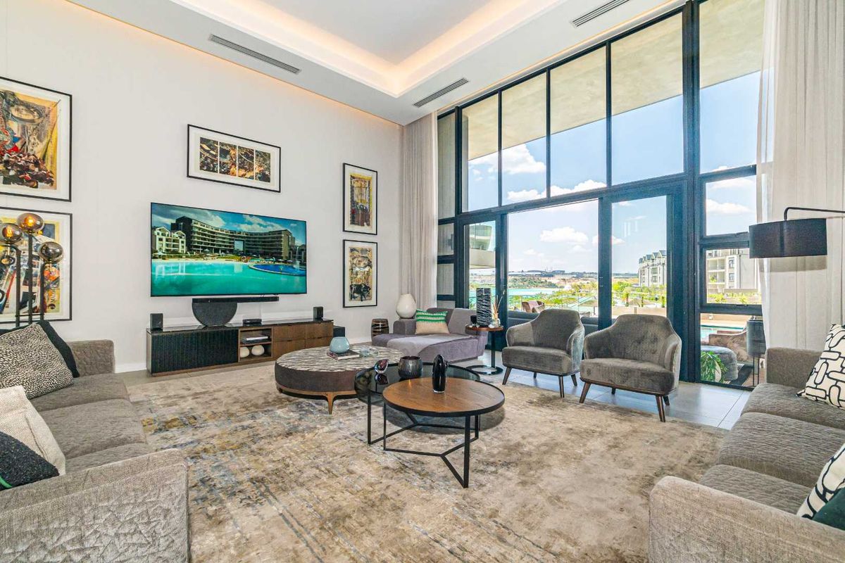 Spacious double-volume living area featuring floor-to-ceiling glass windows, recessed ceiling lighting, and direct access to an outdoor balcony with scenic views.