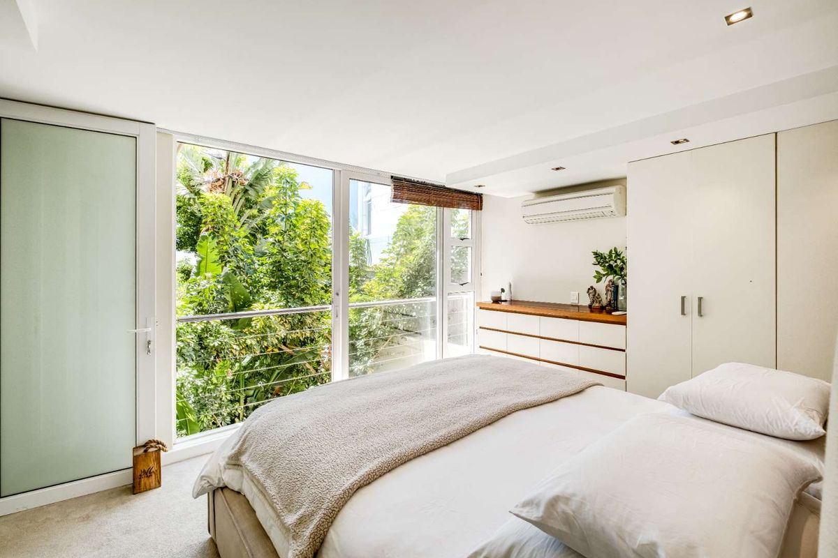 A bright bedroom featuring built-in wardrobes, a wall-mounted air conditioning unit, and large windows overlooking lush greenery.