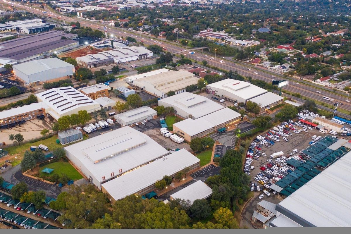 Aerial view of a large industrial park featuring multiple warehouse buildings, extensive paved parking areas with shade structures, and convenient highway access.