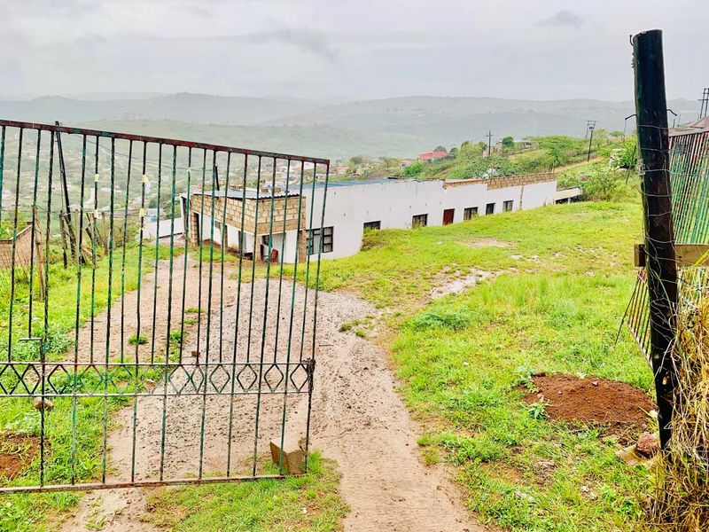 Exterior view of a property featuring a metal security gate, gravel driveway, and unfinished masonry walls set against a hilly landscape.