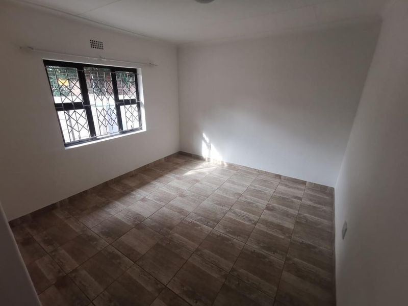 A clean, empty bedroom featuring neutral tiled flooring and a window fitted with security bars, providing a blank canvas for interior design.