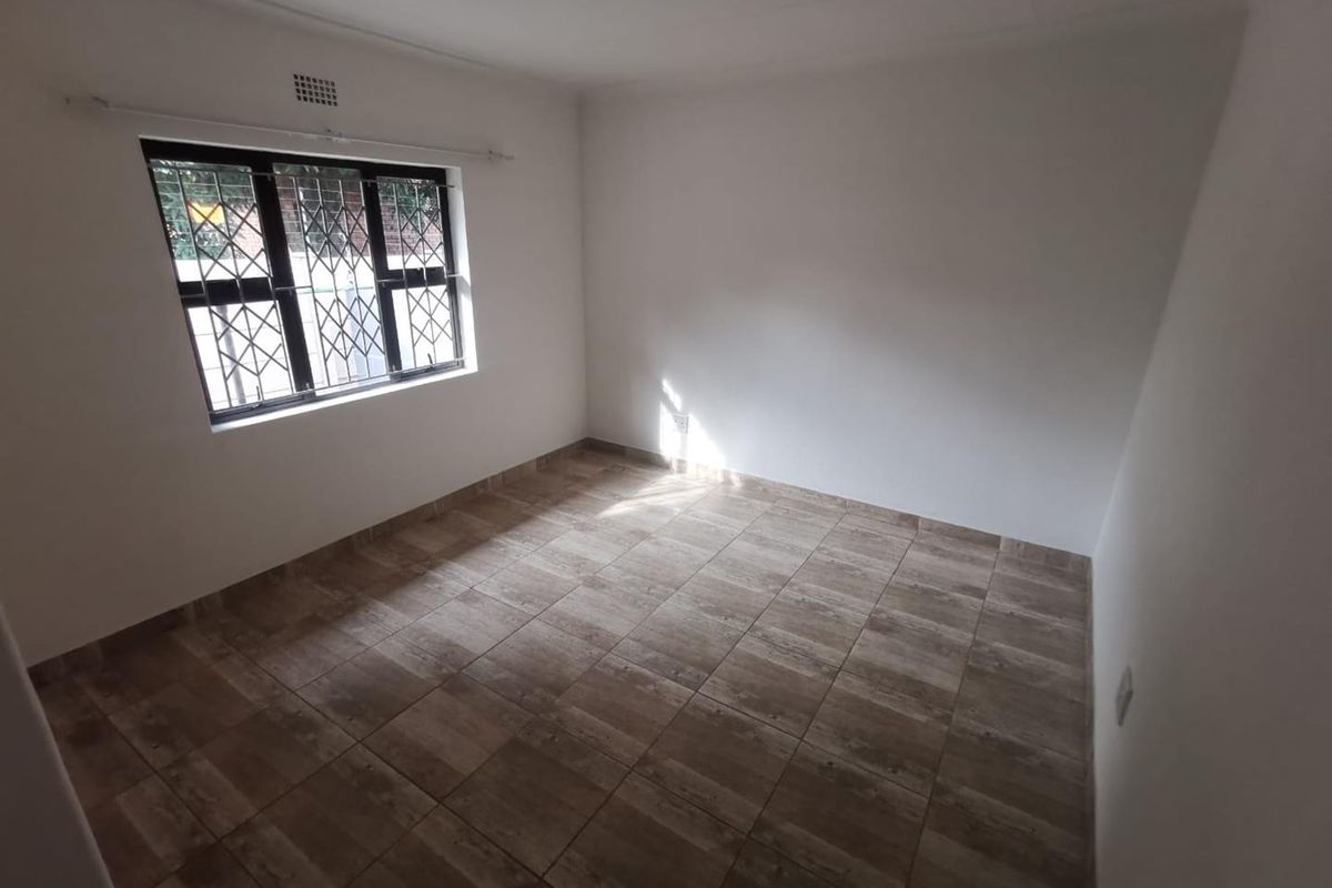 A clean, empty bedroom featuring neutral tiled flooring and a window fitted with security bars, providing a blank canvas for interior design.
