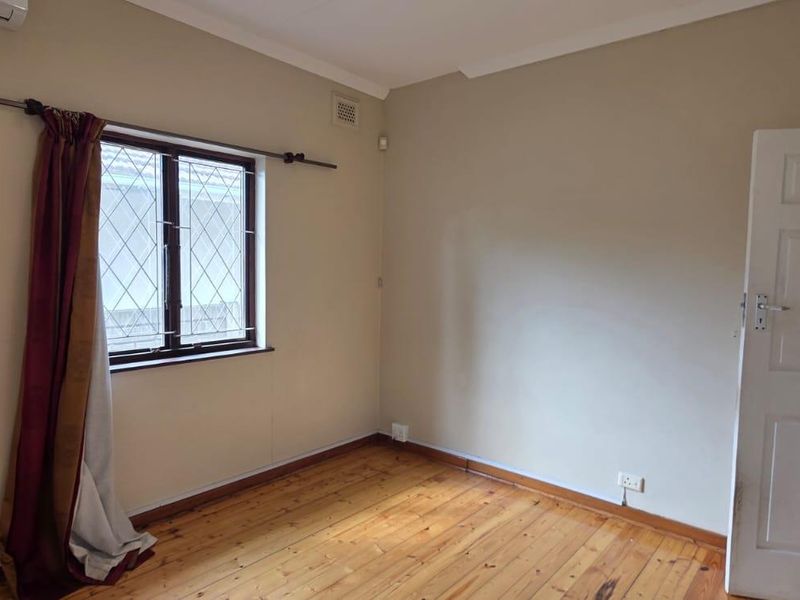 A vacant bedroom featuring original timber flooring, a leaded glass window, and a wall-mounted air conditioning unit.