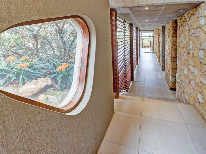 A modern, architecturally designed hallway featuring stone wall cladding, timber louvre shutters, and a unique custom-shaped window overlooking the garden.