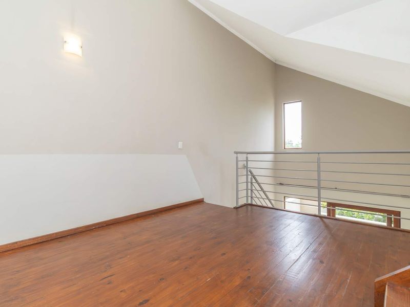 A bright mezzanine level featuring polished timber flooring, high vaulted ceilings, and a modern metal balustrade overlooking the lower living area.