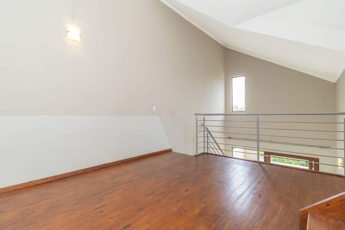 A bright mezzanine level featuring polished timber flooring, high vaulted ceilings, and a modern metal balustrade overlooking the lower living area.