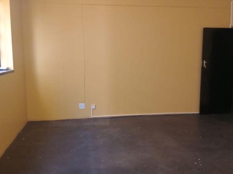 An empty living room featuring yellow painted walls, exposed electrical conduit, and a dark concrete floor finish.