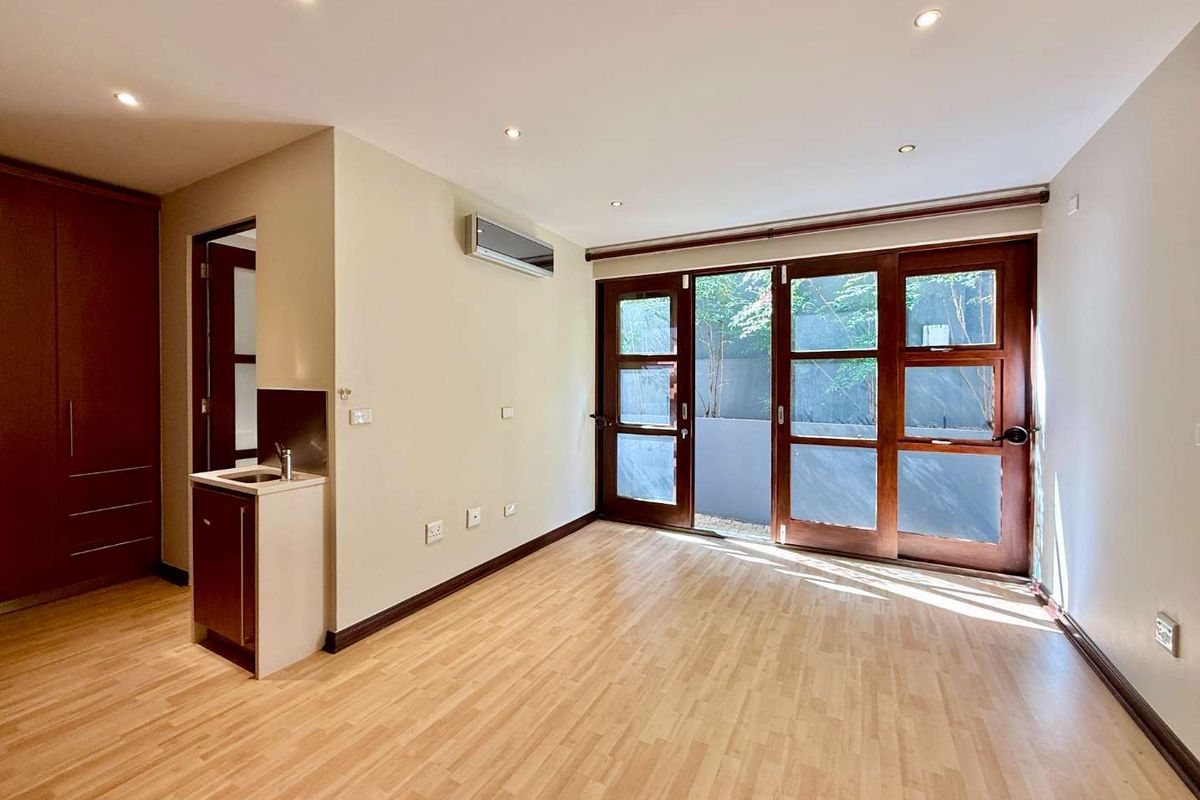 A bright bedroom featuring wood-look flooring, built-in cabinetry, a small kitchenette area, and sliding glass doors opening to a private outdoor space.