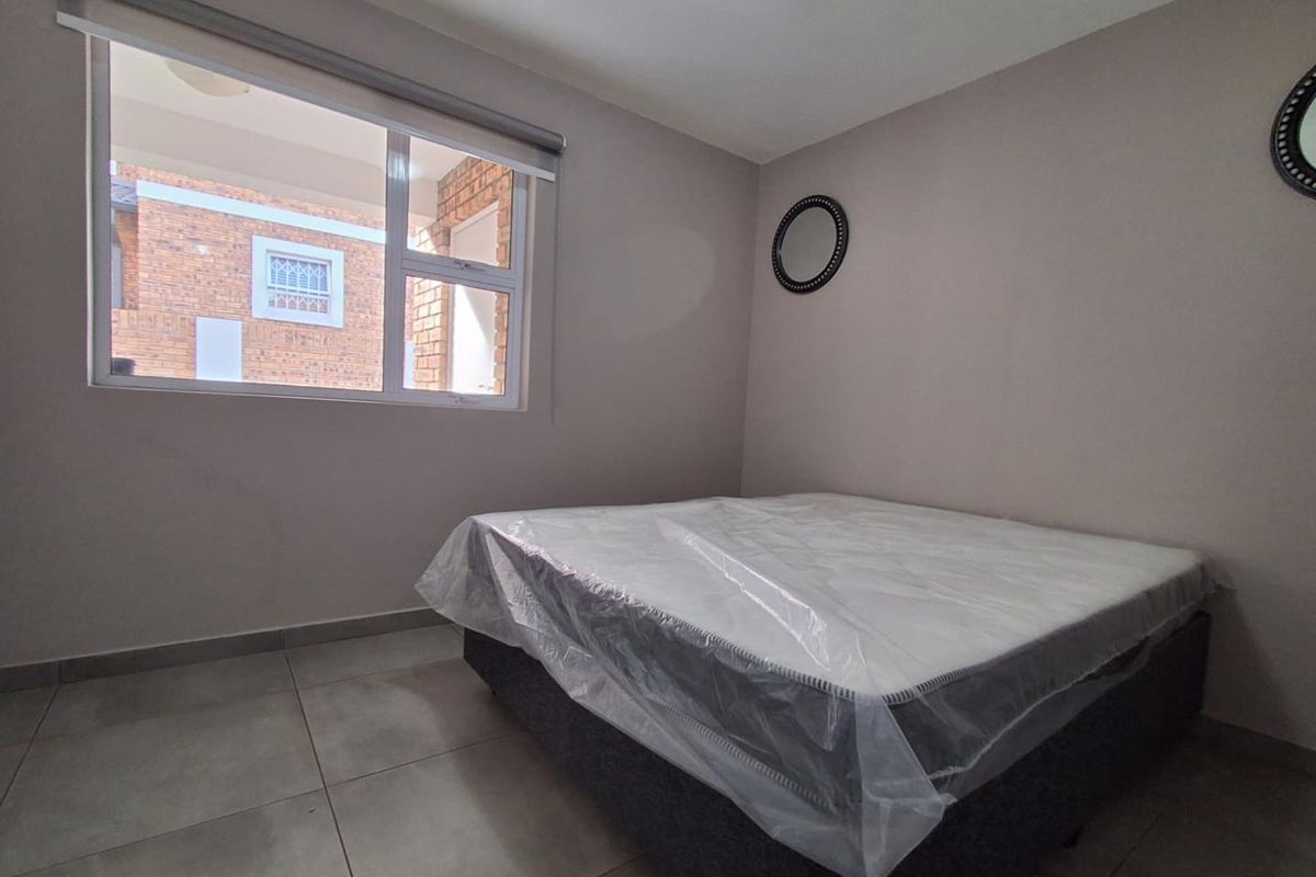 A bedroom featuring neutral wall tones, large format floor tiles, and a window with a roller blind.