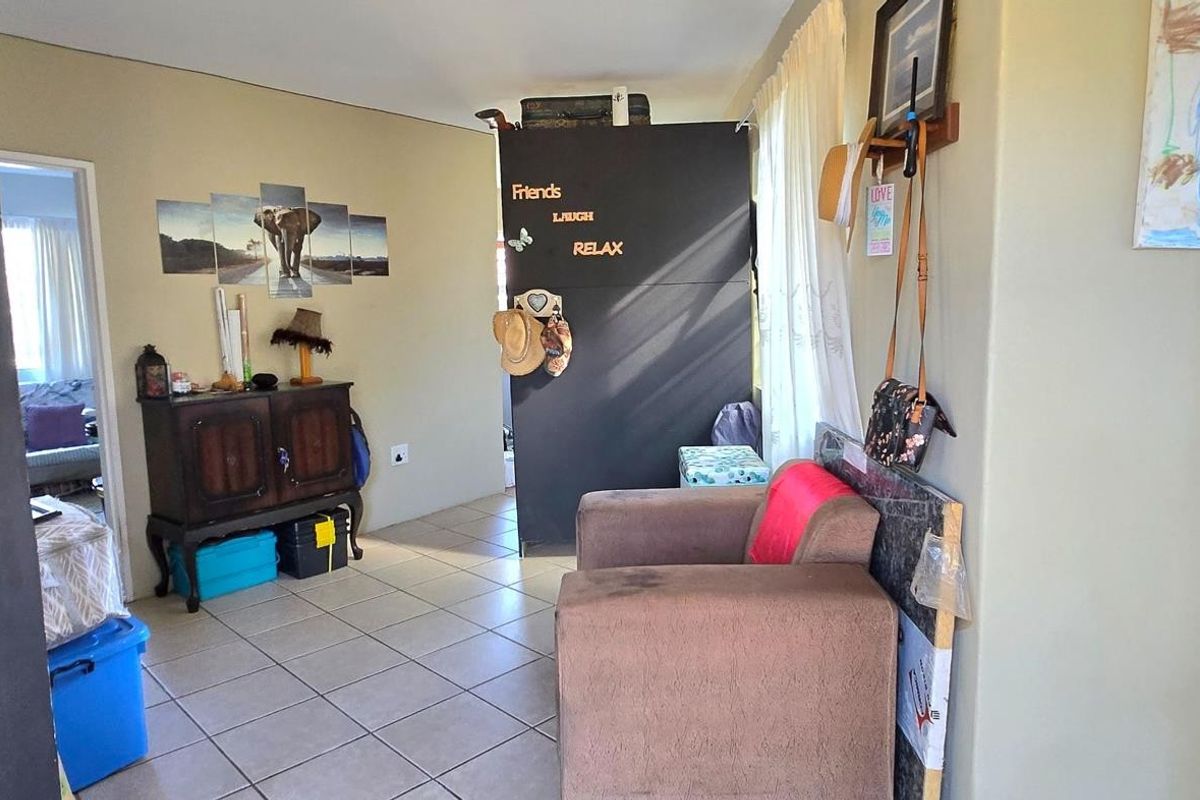 A view of a living area featuring tiled flooring and a partition wall, with an adjacent room visible through the doorway.