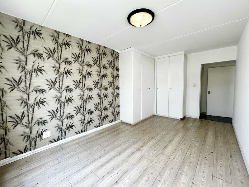 A bright, empty bedroom featuring light-toned laminate flooring, built-in storage cupboards, and a decorative bamboo-patterned feature wall.