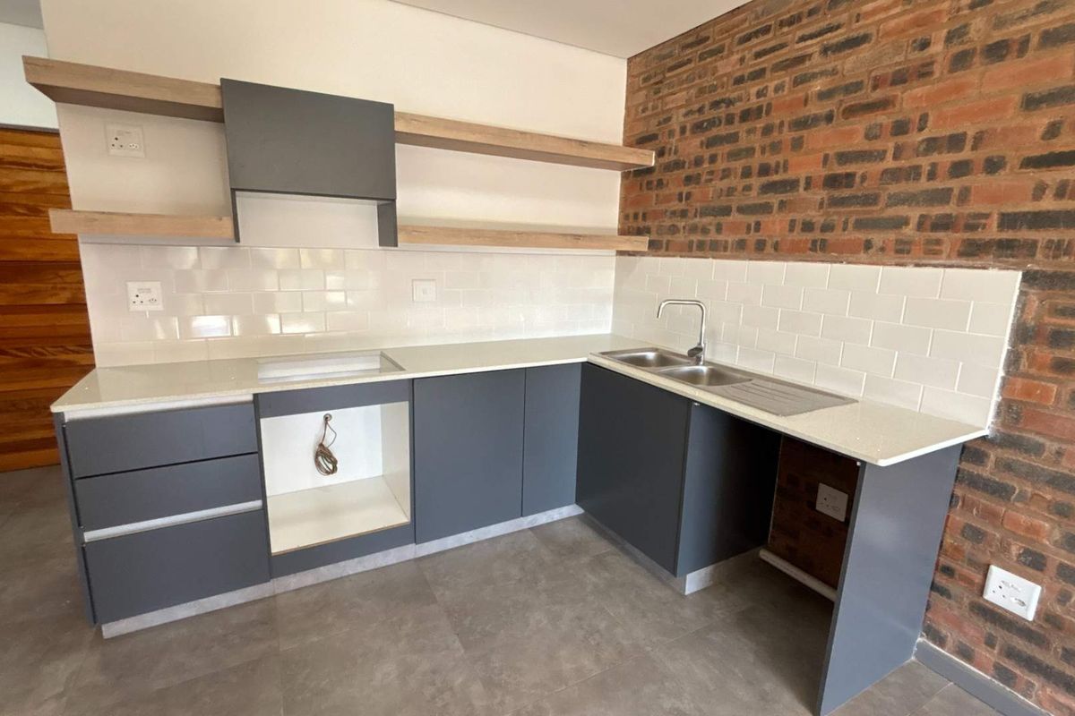 Modern kitchen featuring dark grey cabinetry, light stone countertops, subway tile backsplash, and a distinctive exposed brick feature wall.