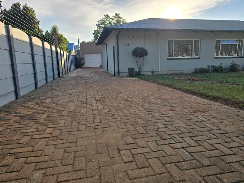 Front exterior view of the property featuring a paved driveway, perimeter wall with electric fencing, and a detached garage.