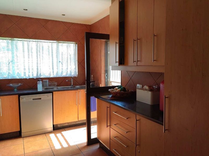A functional kitchen featuring wood-finish cabinetry, dark laminate countertops, tiled backsplash, and tiled flooring with direct access to an outdoor area.