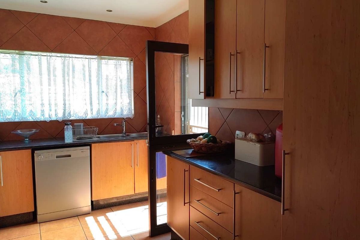 A functional kitchen featuring wood-finish cabinetry, dark laminate countertops, tiled backsplash, and tiled flooring with direct access to an outdoor area.