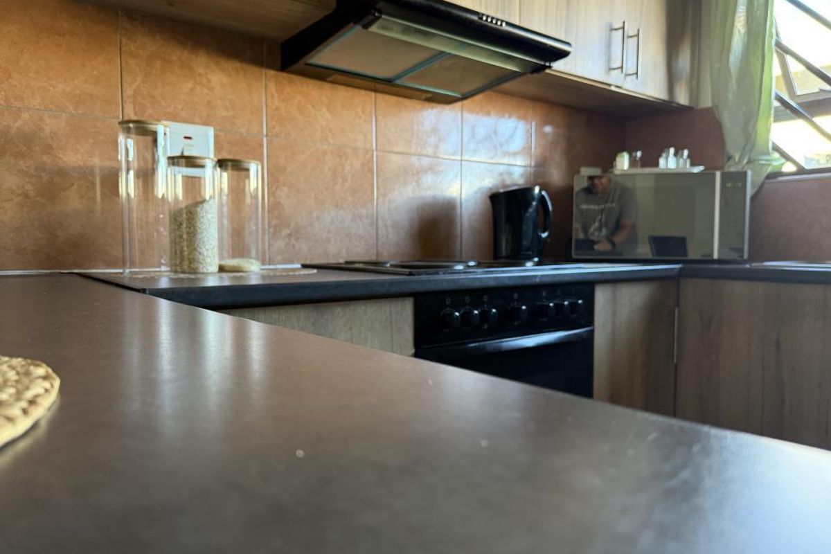 A functional kitchen featuring wood-look cabinetry, dark countertops, a built-in oven, hob, and an extractor fan with tiled splashbacks.
