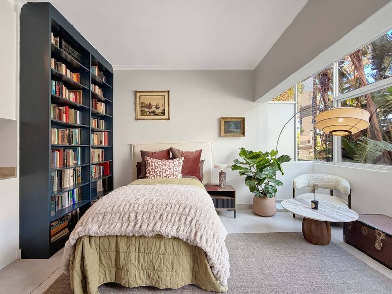 A bright and well-maintained bedroom featuring a large picture window and custom built-in floor-to-ceiling shelving, offering ample storage and natural light.