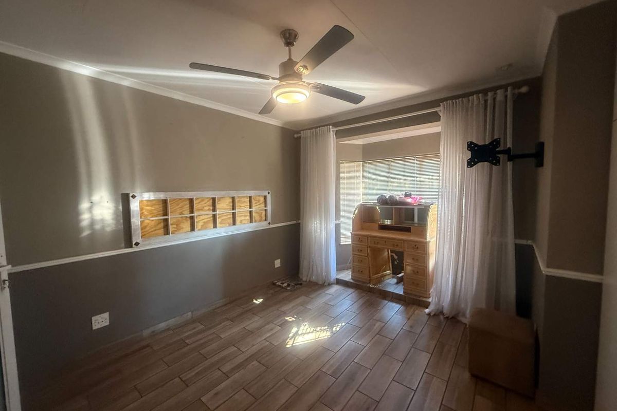 A bedroom featuring tiled flooring, a ceiling fan, and a wall-mounted TV bracket, with a window area providing natural light.
