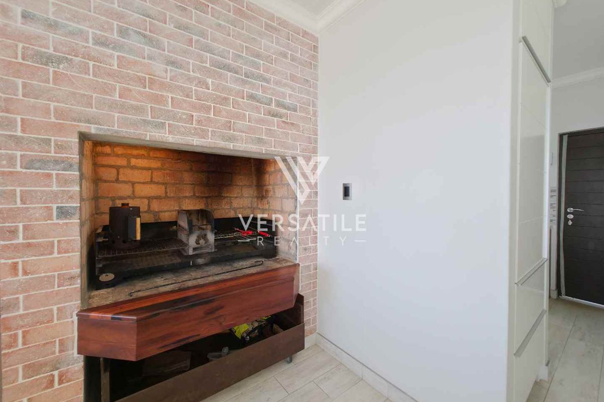 Indoor braai area featuring a brick-clad fireplace with a built-in hearth and chimney, adjacent to a modern door and tiled flooring.