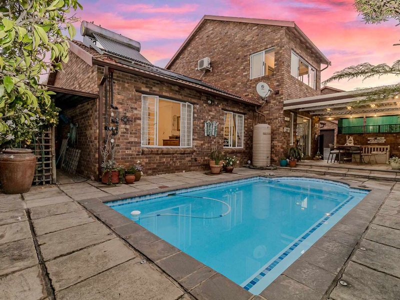 Rear exterior view of a townhouse featuring a swimming pool, paved patio area, solar water heating system, and brick facade.