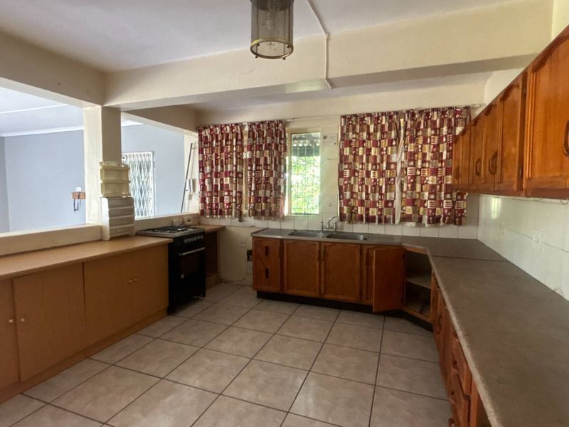 A dated kitchen featuring wooden cabinetry, laminate countertops, and a freestanding stove, offering a functional layout with potential for modern renovation.
