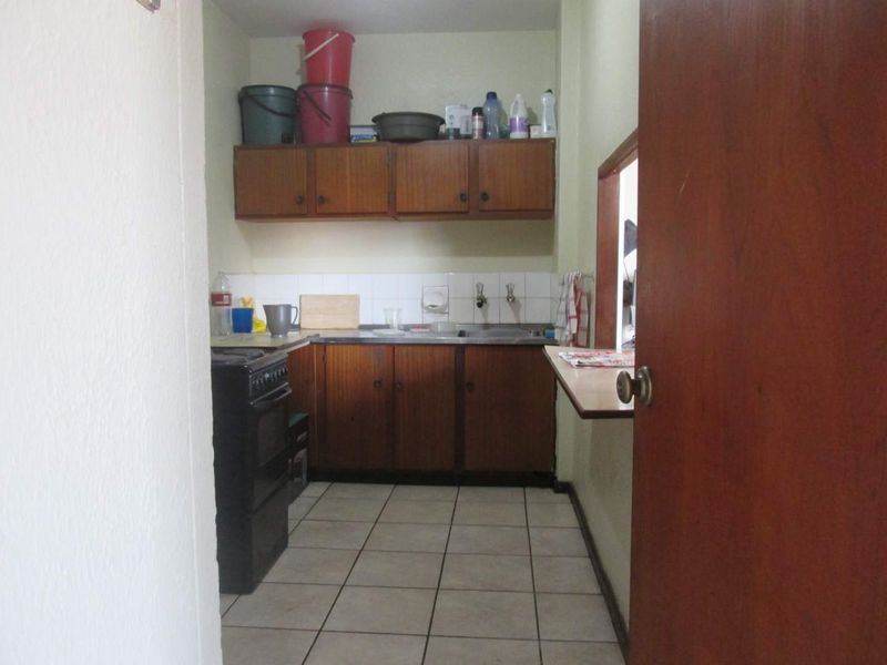 A compact, functional kitchen featuring dated wooden cabinetry, tiled backsplash, and a convenient pass-through window connecting to the adjacent living space.
