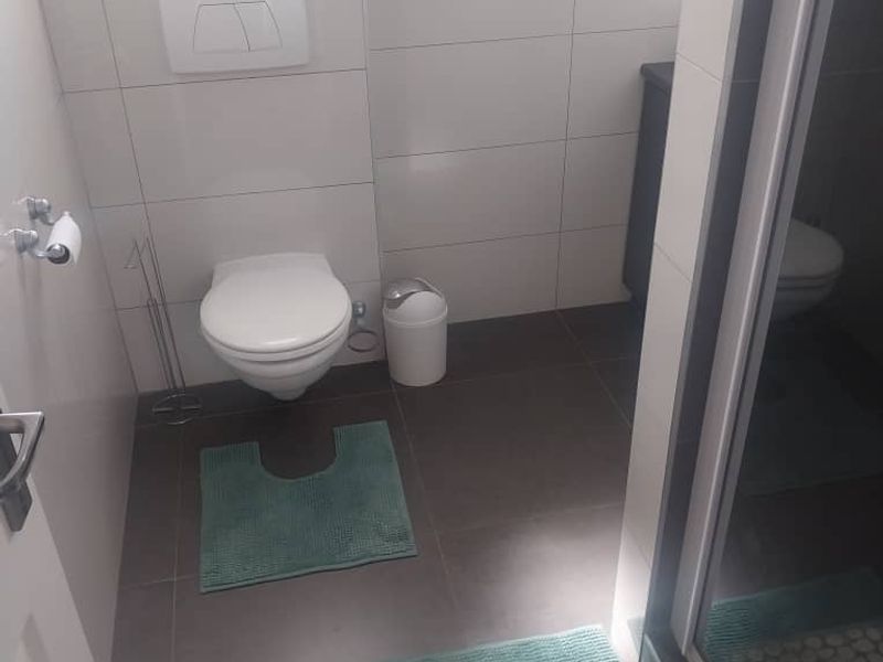 A modern bathroom featuring a wall-mounted toilet with a concealed cistern, tiled walls and flooring, and a glass-enclosed shower area.