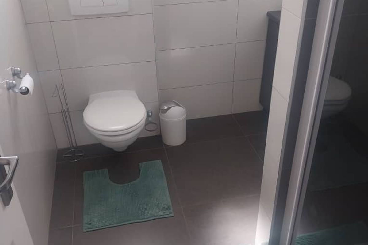 A modern bathroom featuring a wall-mounted toilet with a concealed cistern, tiled walls and flooring, and a glass-enclosed shower area.