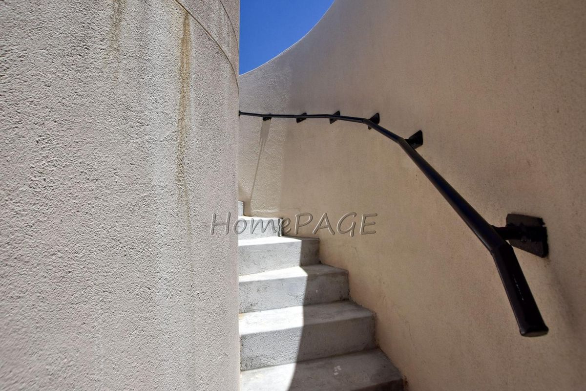 A curved exterior staircase featuring concrete steps and a black metal handrail, leading upwards against a textured wall.