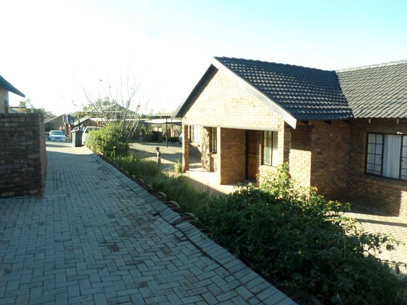 Exterior view of a face brick apartment unit featuring a tiled roof, paved driveway, and established garden area.