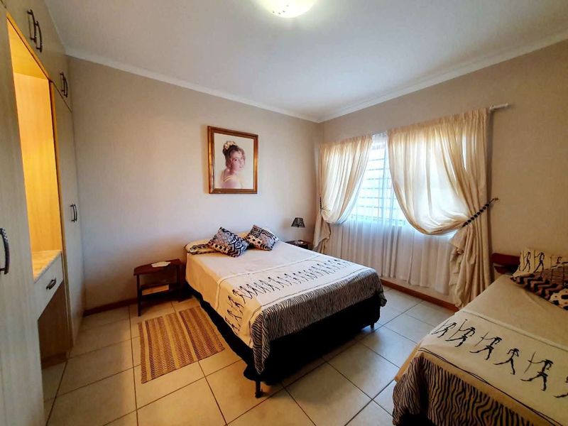 A functional bedroom featuring tiled flooring, built-in cupboards, and security bars on the window, providing a practical and well-lit living space.