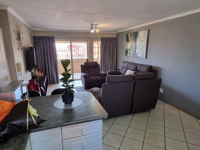 Open-plan living area featuring a kitchen with granite countertops and tiled flooring, leading directly to a balcony through sliding glass doors.