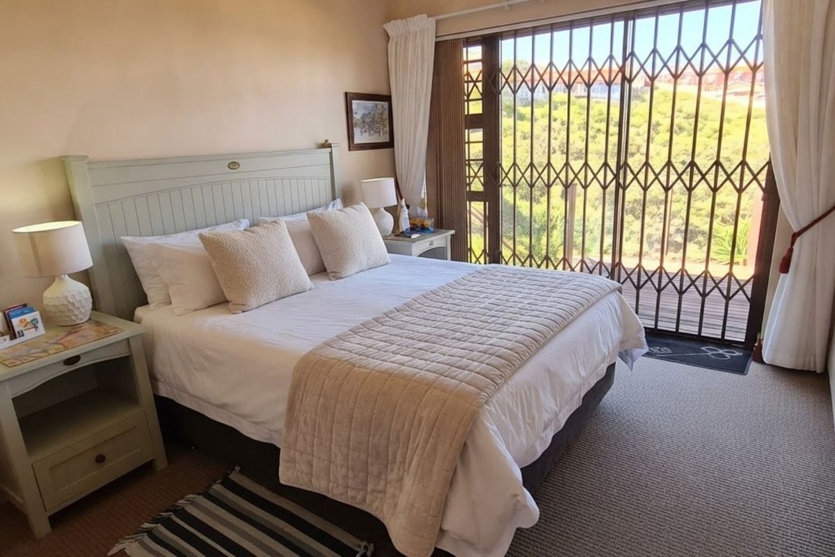 A well-maintained bedroom featuring built-in cupboards, carpeted flooring, and a sliding glass door with a security gate leading to an outdoor area.