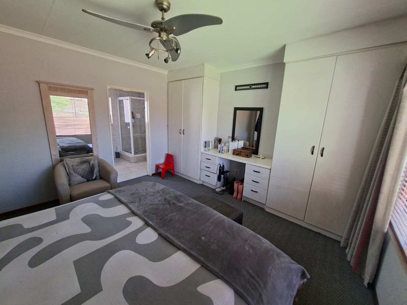 Spacious bedroom featuring built-in cupboards, a ceiling fan, and direct access to an en-suite bathroom with a shower.