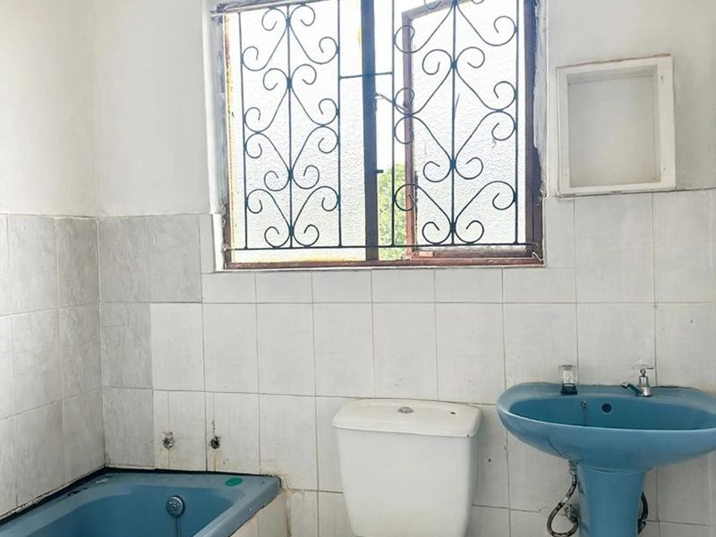 A dated bathroom featuring a blue bathtub and pedestal basin, requiring renovation to update the finishes and address visible tile and maintenance issues.