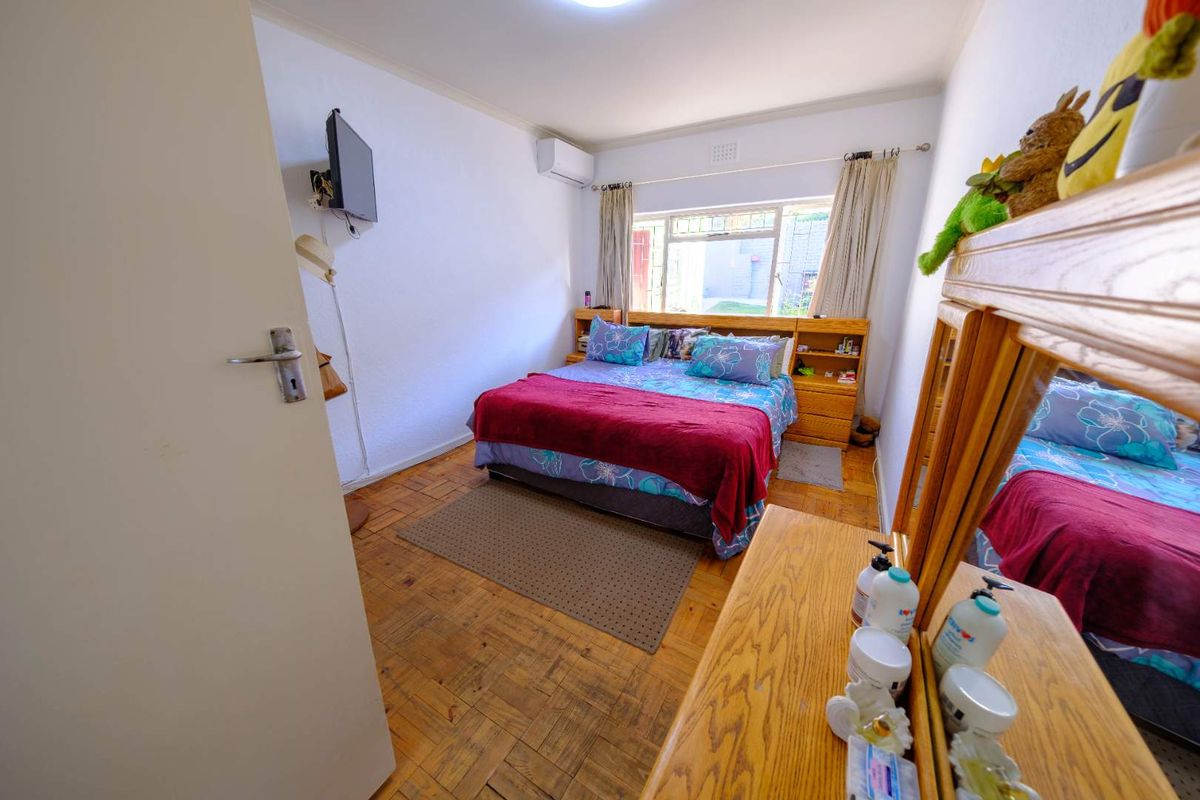 A bedroom featuring parquet flooring, a wall-mounted air conditioning unit, and a built-in headboard with integrated shelving.