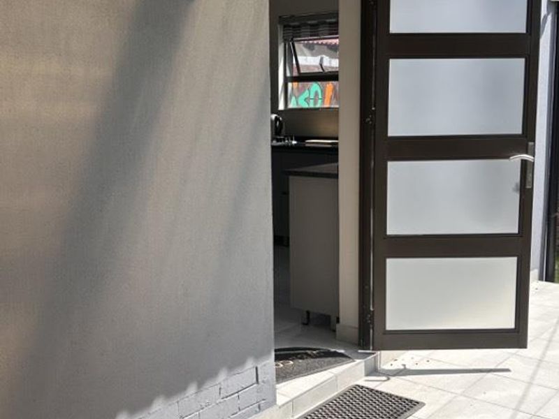 Rear exterior view showing a tiled patio area, brick paving, and a modern frosted glass door leading into the apartment.