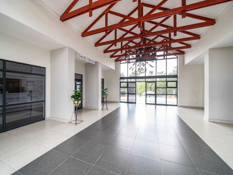 Spacious clubhouse entrance hall featuring high exposed timber roof trusses, large glass windows, and modern tiled flooring.