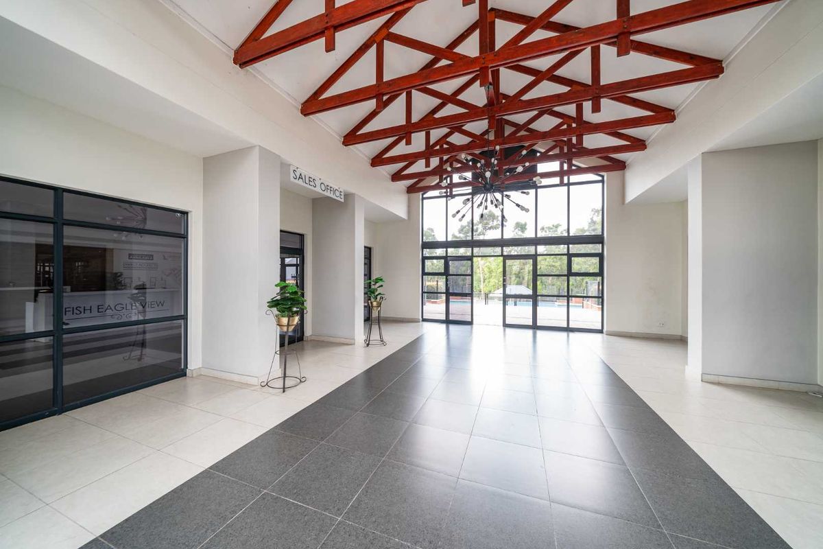 Spacious clubhouse entrance hall featuring high exposed timber roof trusses, large glass windows, and modern tiled flooring.
