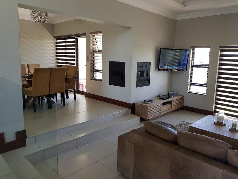 Spacious open-plan living and dining area featuring tiled floors, a built-in fireplace, and large windows with modern blinds.