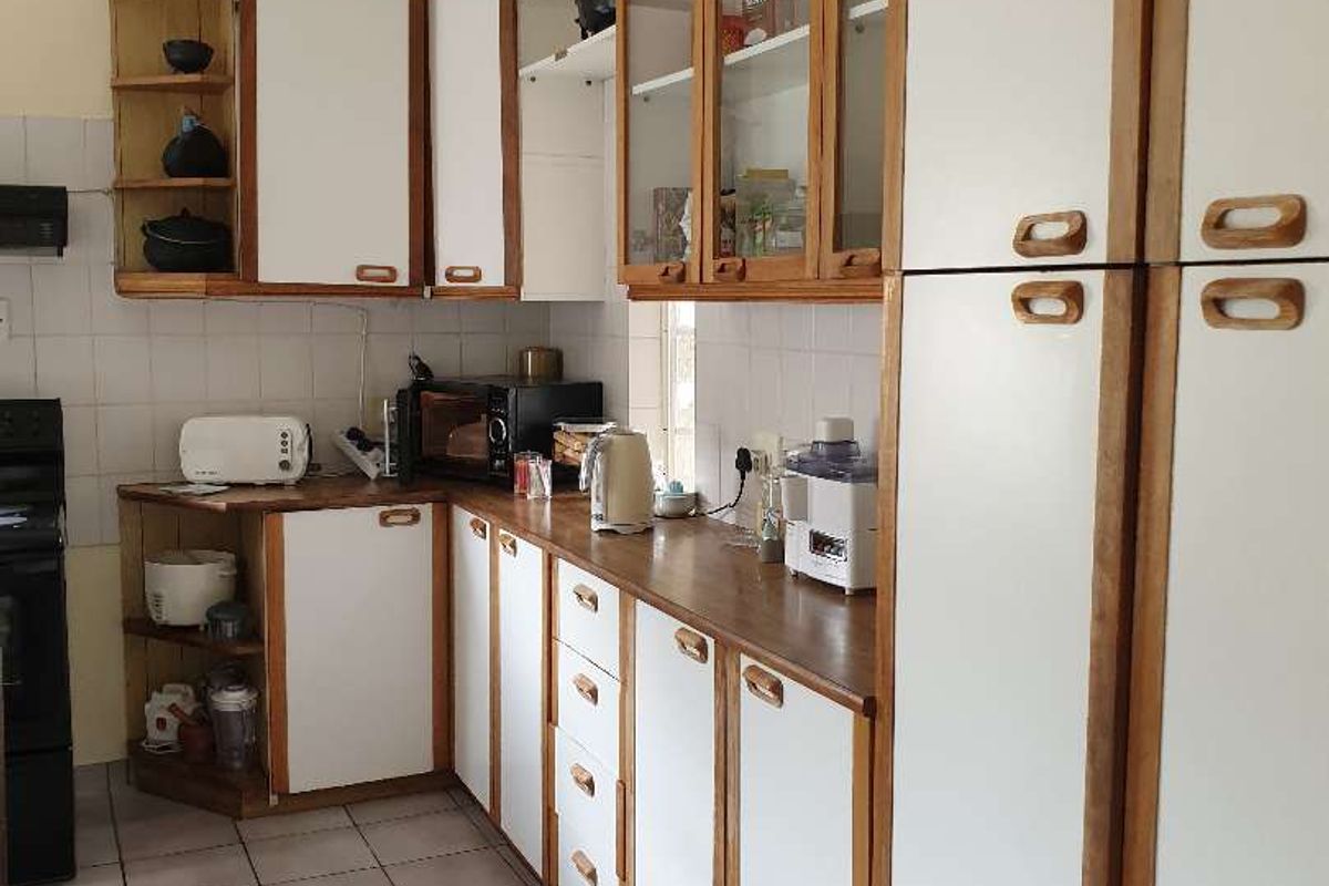 A functional kitchen featuring white cabinetry with wood trim, tiled flooring, and tiled splashbacks, offering ample storage and counter space.