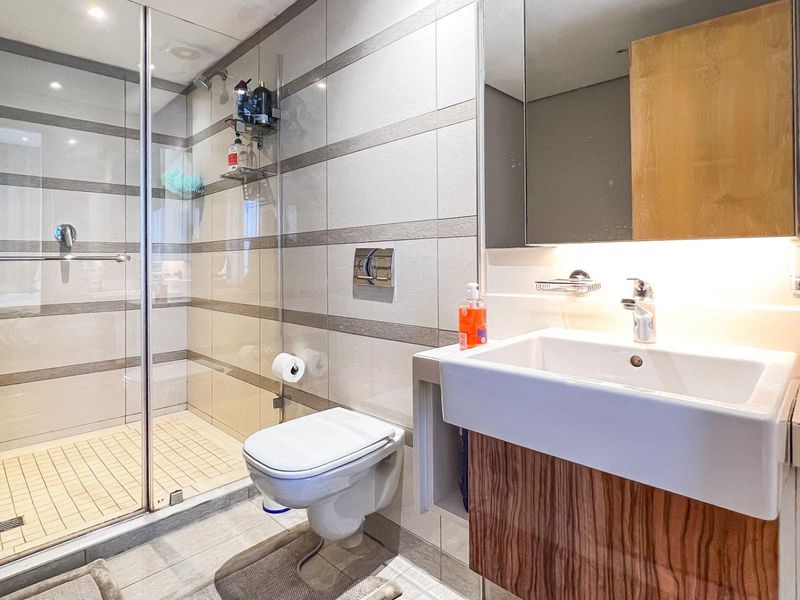 Modern bathroom featuring a wall-mounted toilet, glass-enclosed shower, and a sleek vanity unit with integrated basin and mirror.